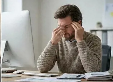 Man at his desk pressing his sinuses from facial pressure, a sign of granulomatosis with polyangiitis